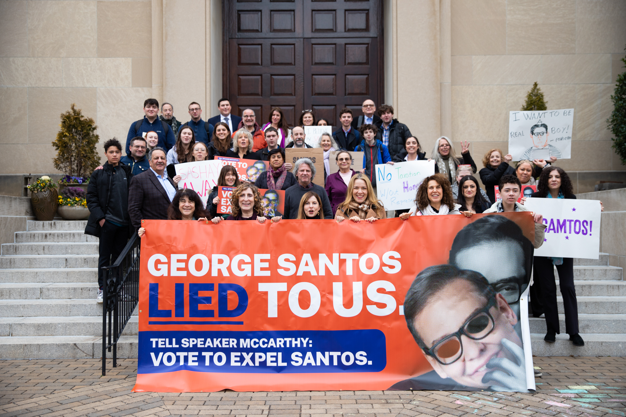 Constituents of Rep. Santos hold signs saying, 